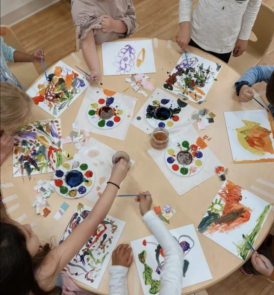 Group of young children seated around a circular table painting with watercolors at Ivybrook Academy Apex