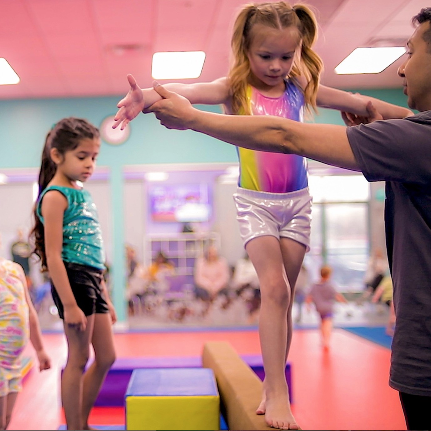 Young girl practicing balance on a gymnastics beam with an instructor's support at Little Gym of North Raleigh/Wake Forest